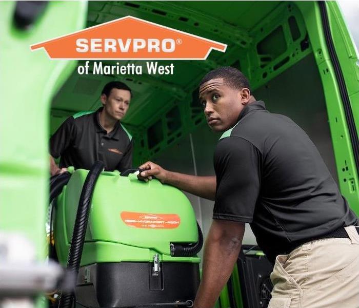 two SERVPRO employees unloading cleaning equipment out of a Green truck  